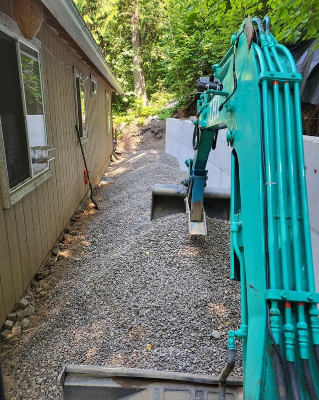 excavator spreading gravel by a retaining wall